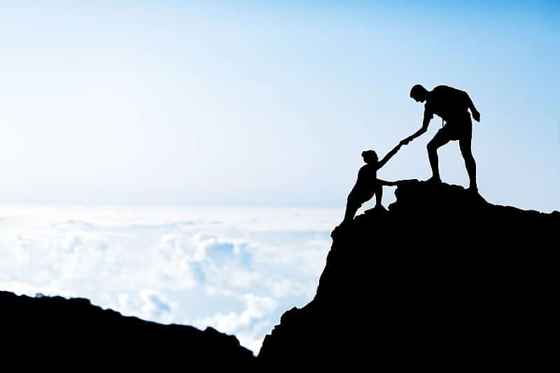 Image of a man helping a woman up a mountain. Image by Baloghabalazs